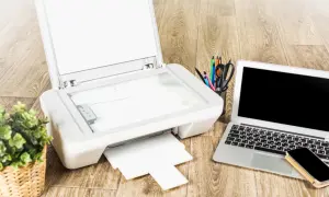 Drukarka HP, laptop, telefon i koszyk z przyborami na drewnianym tle.