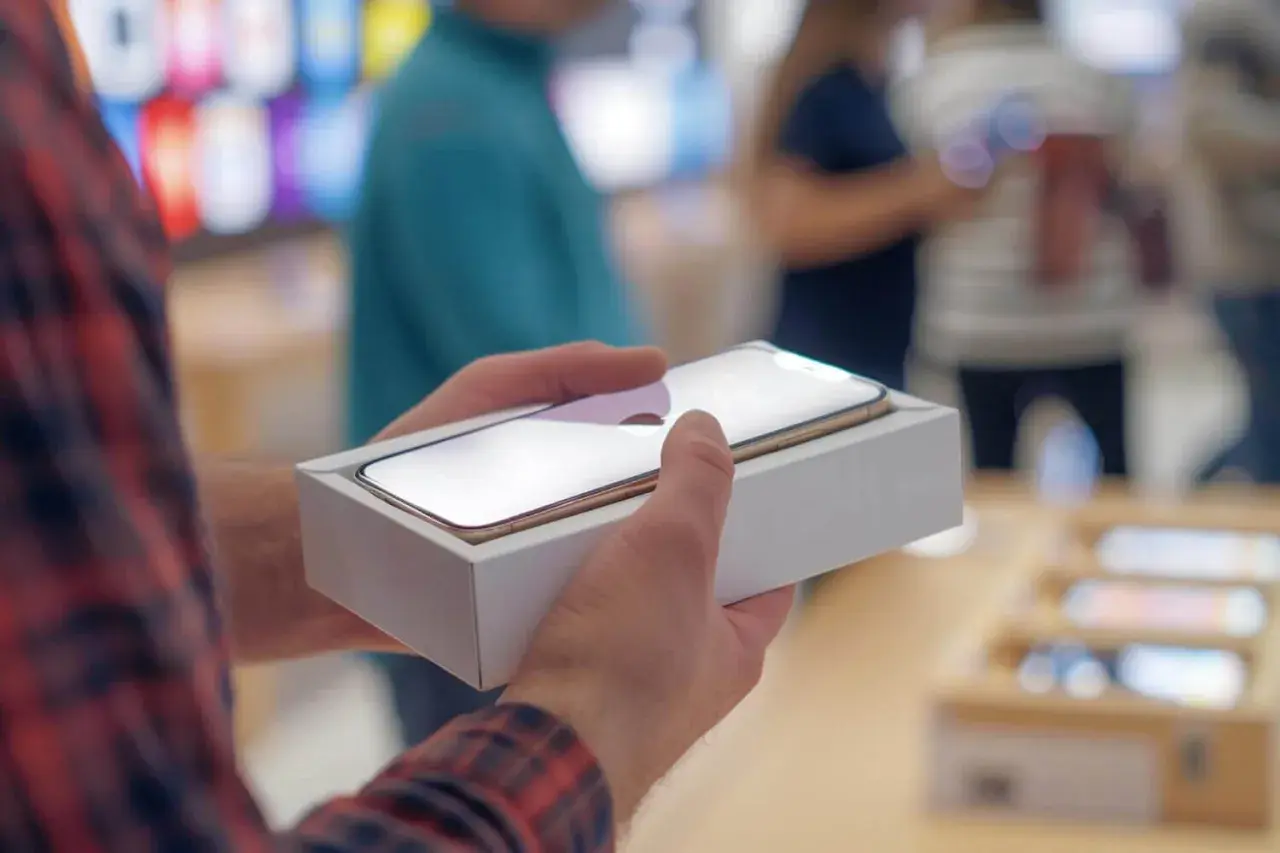 Mężczyzna trzyma nowe iPhone w pudełku, gotowy do podróży. Dowiedz się, jak włączyć roaming iPhone, by pozostać w kontakcie za granicą.