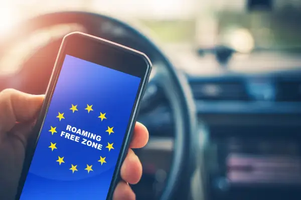 Dłoń trzyma smartfon z flagą UE i napisem "ROAMING FREE ZONE". Dowiedz się, jak włączyć roaming w Play, by podróżować bez dodatkowych kosztów.